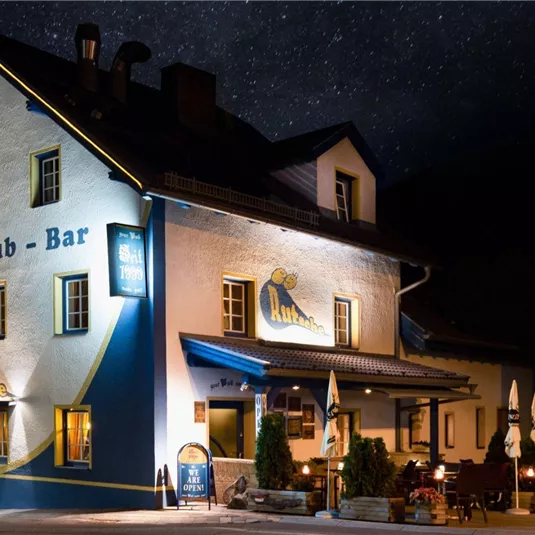 Ein charmantes Gebäude mit der Aufschrift „Pub - Bar“ in einer nächtlichen Umgebung. Es ist beleuchtet und lädt zum Verweilen ein.