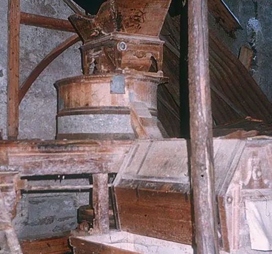 Eine alte Mühle mit hölzernen Komponenten und steinernen Wänden. Der Raum wirkt unbenutzt und antiquiert.