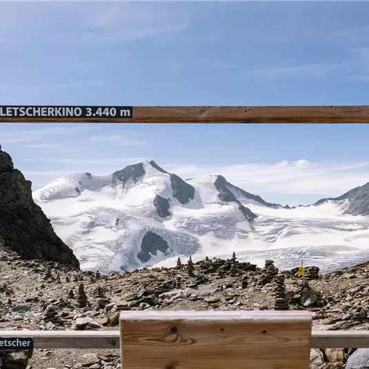 A breathtaking view of snow-covered mountains through a wooden frame. The image showcases the glacier landscape at an altitude of 3,440 meters.