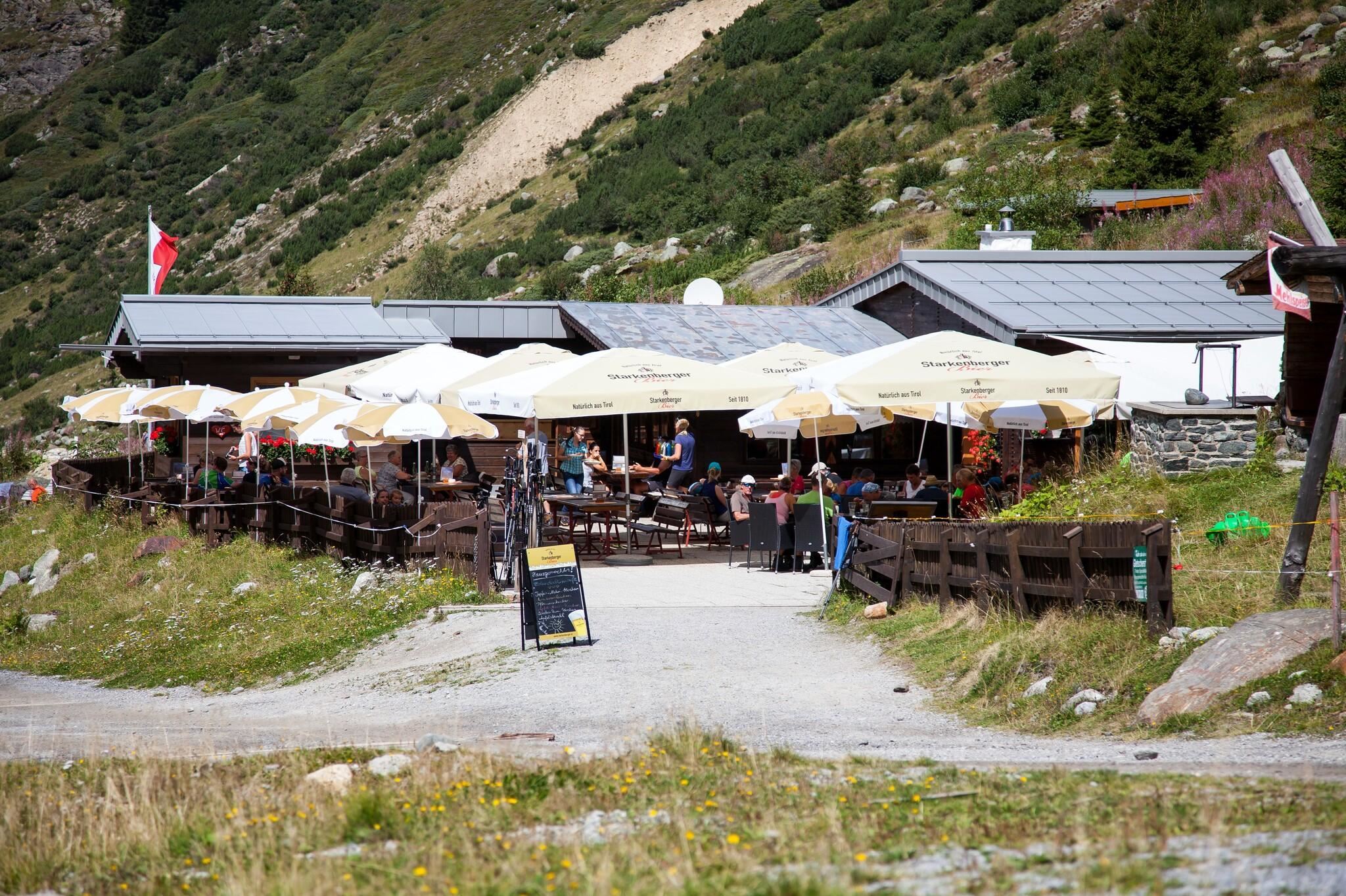 Ein gemütliches Restaurant in den Bergen mit sonnigen Terrassen und Sonnenschirmen. Viele Leute genießen die frische Luft und die schöne Umgebung.