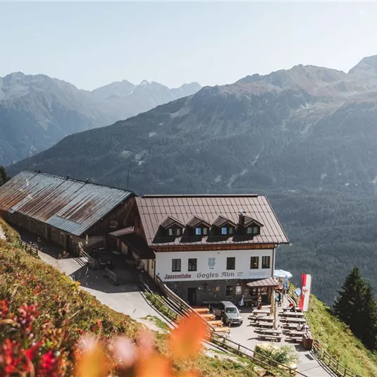 Eine Berghütte umgeben von beeindruckenden Bergen und rotem Herbstlaub. Der Himmel ist klar und die Aussicht ist atemberaubend.