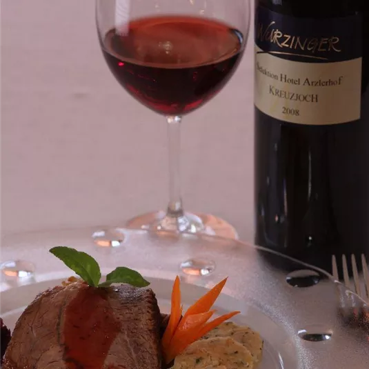 Ein köstliches Gericht aus zartem Fleisch mit Sauce, serviert mit einer Beilage und frischen Karotten. Dazu ein Glas roten Wein und eine Flasche des gleichen Weins.