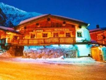 Ein gemütliches Chalet im winterlichen Bergdorf, beleuchtet in sanften Farben. Schnee bedeckt den Boden und die Berge sind im Hintergrund sichtbar.