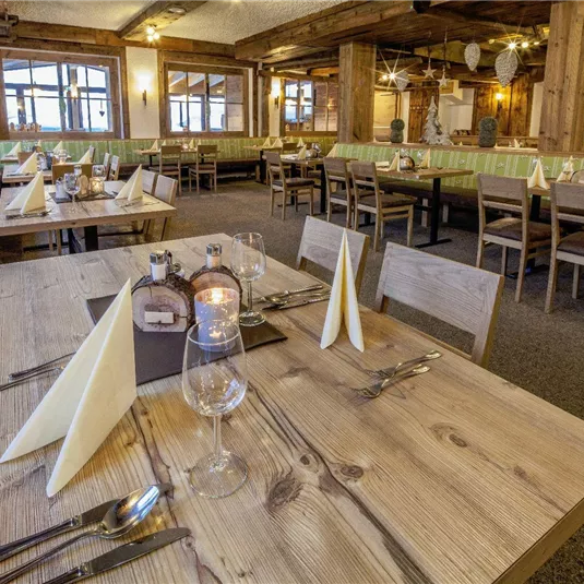 Ein gemütliches Restaurant mit holzverkleideten Wänden und Tischen aus hellem Holz. Die Tische sind elegant gedeckt mit Besteck und Gläsern.