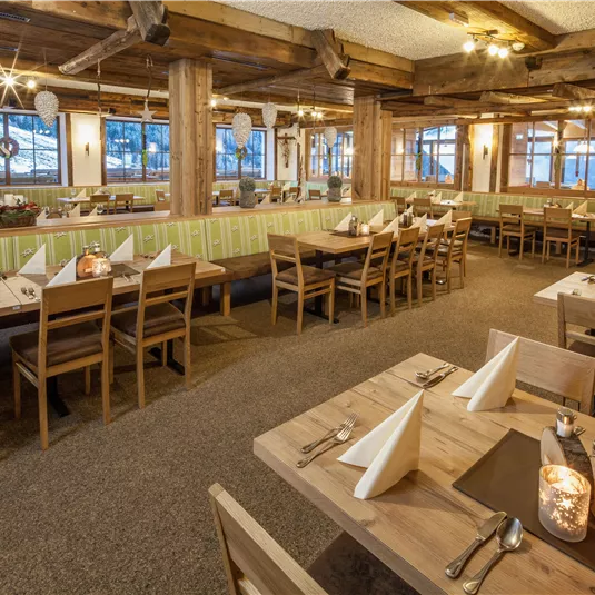 Ein gemütliches Restaurant mit Holzmöbeln und einem warmen Ambiente. Tische sind sorgfältig gedeckt und große Fenster bieten einen Blick nach draußen.