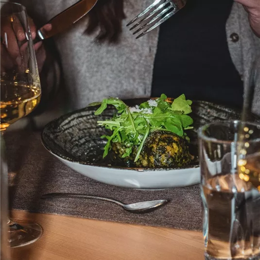 Ein Teller mit einer köstlichen Mahlzeit in einem eleganten Restaurant. Eine Person hält Besteck und bereit sich darauf vor, das Essen zu genießen.
