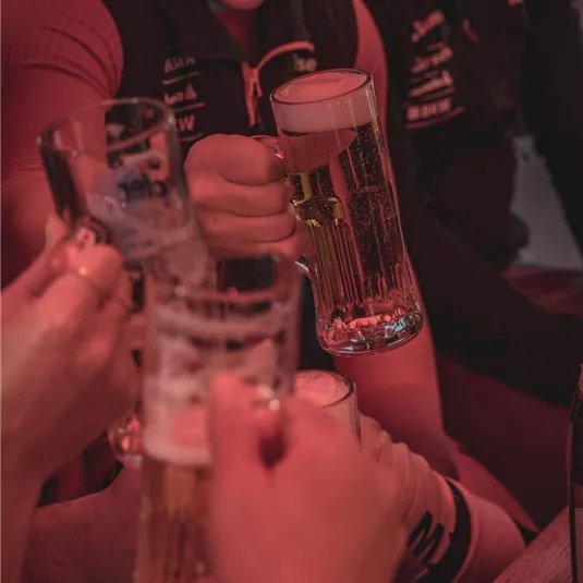 Eine Gruppe von Menschen stößt mit Bierkrügen an. Sie sitzen in einem geselligen Ambiente und haben viel Spaß.