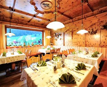Ein gemütliches Restaurant mit Holzverkleidung und warmem Licht. Die Tische sind schön gedeckt und bieten einen Blick auf die natürliche Umgebung.