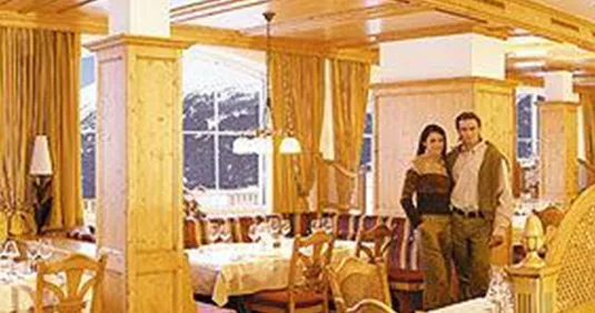 Ein einladendes Restaurant mit Holzdekor und eleganten Tischen. Im Hintergrund sind schneebedeckte Berge durch große Fenster sichtbar.