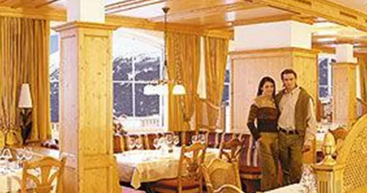 Ein gemütliches Restaurant mit Holzmöbeln und eleganten Tischdecken. Im Hintergrund sind die schneebedeckten Berge sichtbar.