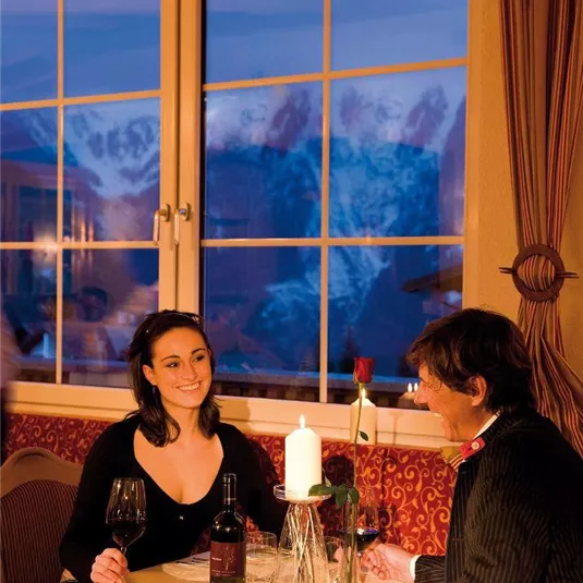 Ein romantisches Abendessen bei Kerzenlicht mit Blick auf die Berge. Das Paar genießt Wein und eine gemütliche Atmosphäre.