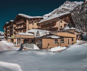 A cozy hotel in the Alps, surrounded by snow-covered mountains. The sky is clear, and the landscape offers a wintery idyll.