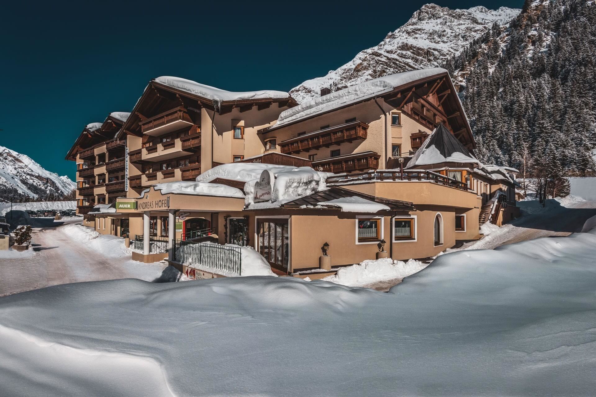 Ein gemütliches Hotel in den Alpen, umgeben von schneebedeckten Bergen. Der Himmel ist klar und die Landschaft bietet eine winterliche Idylle.