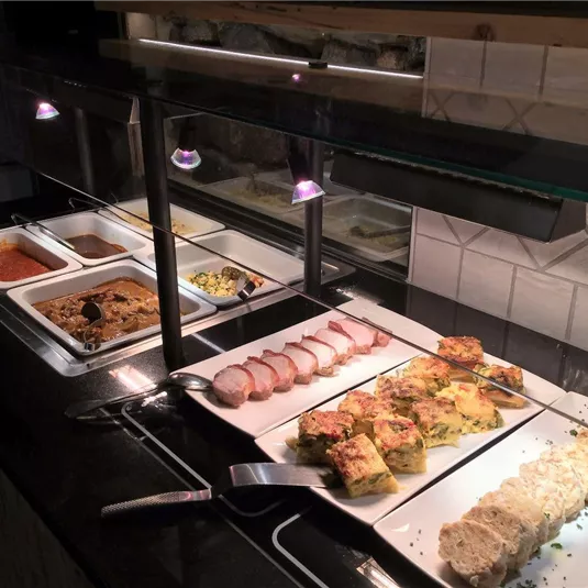 Ein Buffet mit verschiedenen Speisen, darunter Fleisch, Aufläufe und Beilagen. Die Gerichte sind sauber angerichtet und gut beleuchtet.