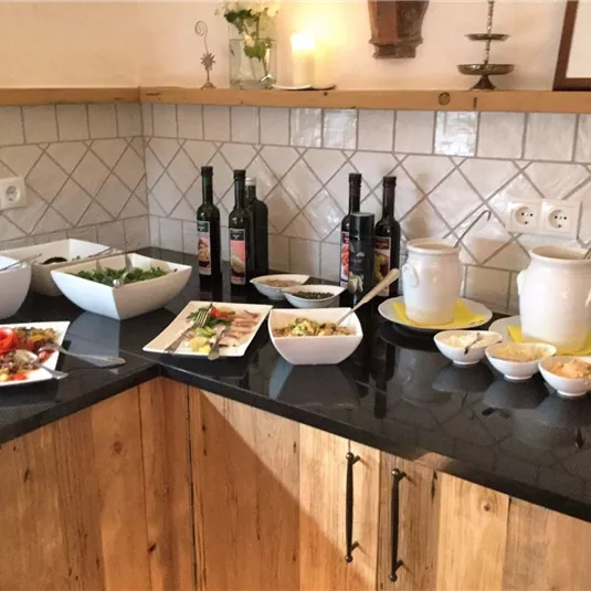 Ein Buffet mit verschiedenen Salaten und Gerichten auf einem dunklen Tisch. Im Hintergrund stehen Flaschen Wein und Geschirr.