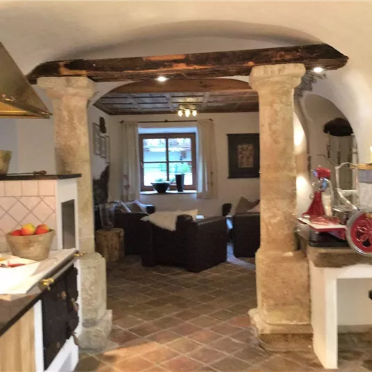 Eine gemütliche Küche mit rustikalem Charme und Steinpfeilern. Im Hintergrund ist ein Wohnzimmer mit einem bequemen Sofa zu sehen.