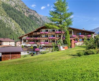 Ein charmantes Berghotel mit Balkonen und bunten Blumen. Umgeben von grünen Wiesen und majestätischen Bergen.
