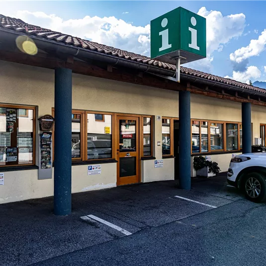 A modern building with large windows and a green sign.
In front of the entrance, there is a white car and the surroundings are bright and inviting.