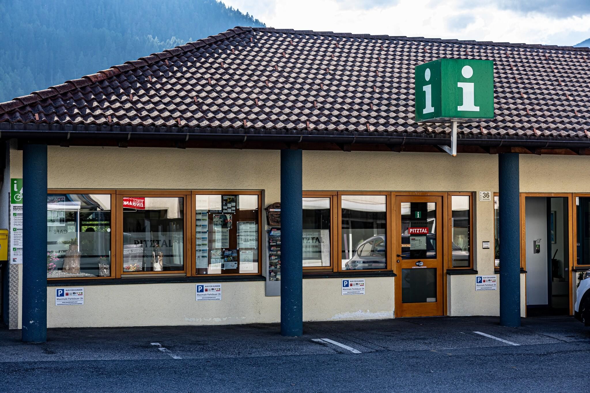 An information center with a greened roof and large windows. The sign above the entrance displays an "i" for information.