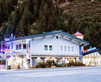 Ein modernes Skigeschäft mit auffälligen Schildern in den Alpen. Umgeben von Bäumen und Bergen bietet es Equipment und Dienstleistungen für Wintersportler an.