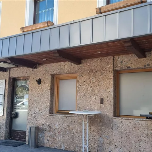 Ein Gebäude mit einer Steinfassade und Holzveranda. Die Fenster sind teilweise geschlossen, und es gibt Tische im Außenbereich.