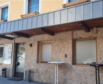 Ein Gebäude mit einer steinernen Fassade und Holzverkleidung. Die Fenster sind leer und es gibt einen kleinen Tisch draußen.