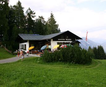 A cozy mountain restaurant surrounded by green meadows. Colorful sun umbrellas stand on the terrace and visitors enjoy the view.