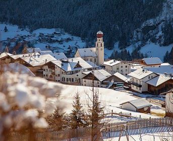 A picturesque village in the snow with traditional houses. In the background, a church tower rises into the blue sky.