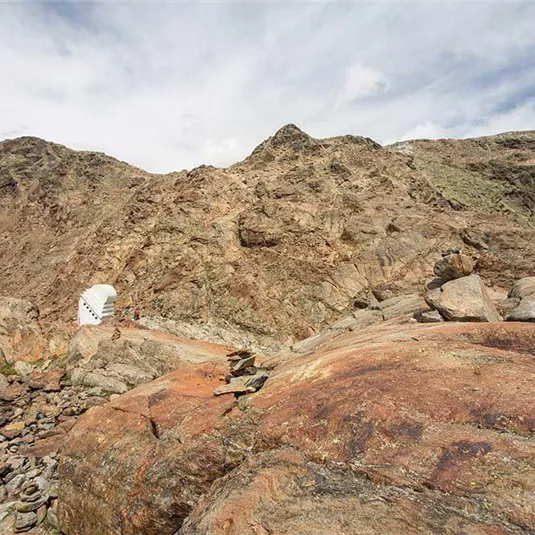 Eine felsige Landschaft mit steilen Hügeln und großen Steinen. Der Himmel ist teilweise bewölkt und die Natur wirkt unberührt.