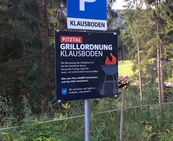 Ein Parkplatzschild mit der Aufschrift "Klausboden" steht in einer bewaldeten Umgebung. Darunter befindet sich ein Schild mit Grillordnungen für den Bereich Klausboden.