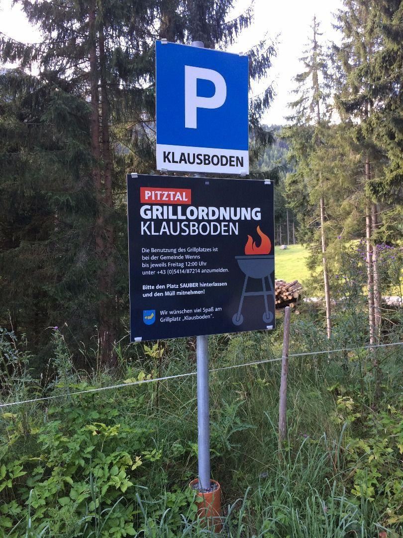 Ein Parkplatzschild mit der Aufschrift "Klausboden" steht in einer bewaldeten Umgebung. Darunter befindet sich ein Schild mit Grillordnungen für den Bereich Klausboden.