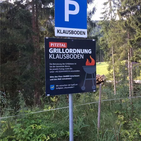 Ein Parkplatzschild mit der Aufschrift "Klausboden" steht in einer bewaldeten Umgebung. Darunter befindet sich ein Schild mit Grillordnungen für den Bereich Klausboden.