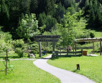 A green meadow with a path and trees. In the foreground stands a sign that reads "Kneippanlage Pitztal".