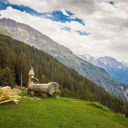A picturesque mountain landscape with lush forests and gentle hills. In the foreground, cozy lounge chairs are on the meadow.