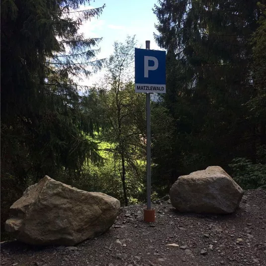 Ein Parkplatzschild befindet sich zwischen zwei großen Steinen im Wald. Im Hintergrund sind grüne Bäume und Licht sichtbar.