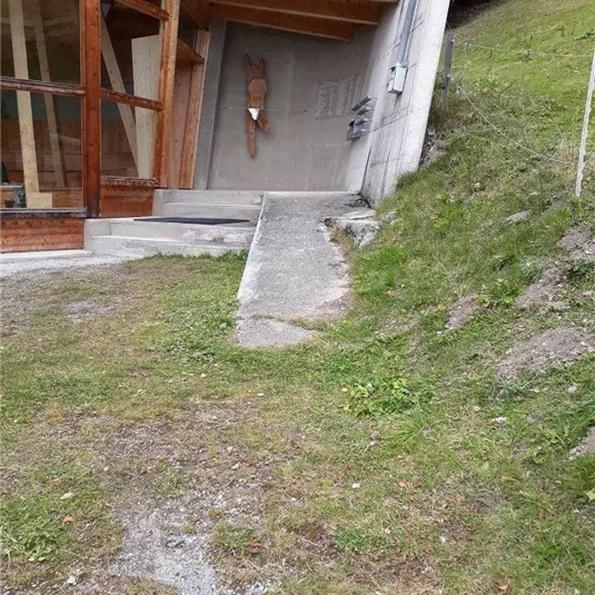 Ein moderner Holzbau mit großen Fenstern. Der Weg führt von der Struktur hinunter zu einer grünen Wiese.