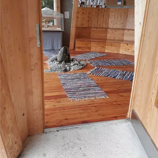 Ein einladender Raum mit Holzfußboden und dekorativen Teppichen. In der Mitte befindet sich ein Steinhaufen, umgeben von Kies.