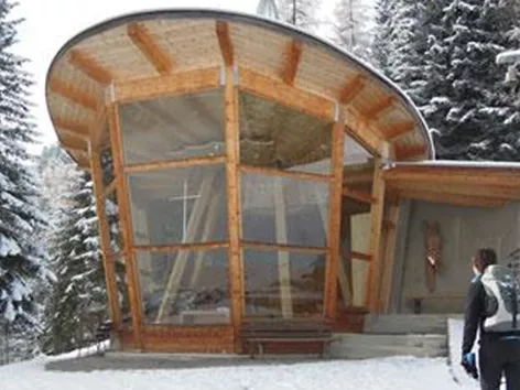 Ein modernes Gebäude in den Bergen, umgeben von schneebedeckten Bäumen. Eine Person geht auf den Eingang zu.