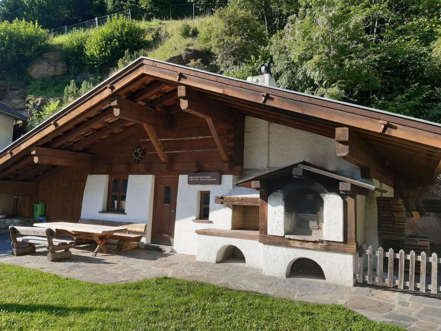 Ein wunderschönes traditionelles Holzhaus mit einer Terrasse und einem Grillbereich. Umgeben von grüner Landschaft und Bäumen.