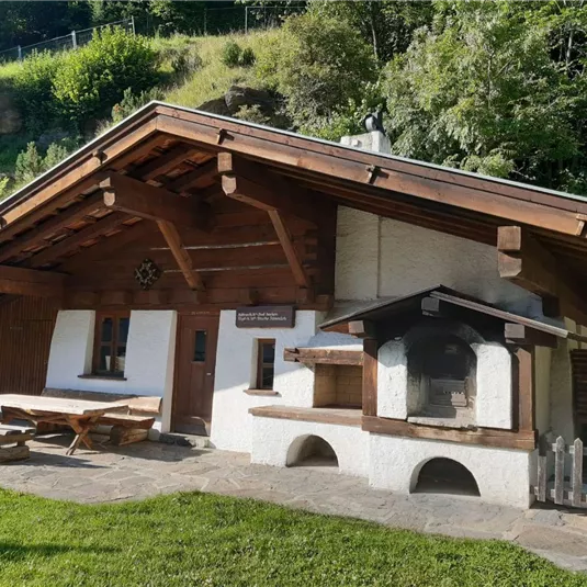 Ein wunderschönes traditionelles Holzhaus mit einer Terrasse und einem Grillbereich. Umgeben von grüner Landschaft und Bäumen.
