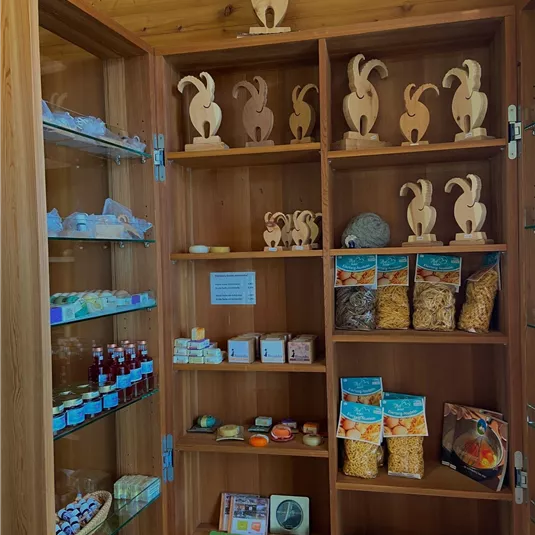 Ein Holzregal mit verschiedenen handgefertigten Produkten. Es sind Figuren, Seifen, Lebensmittel und Getränke zu sehen.