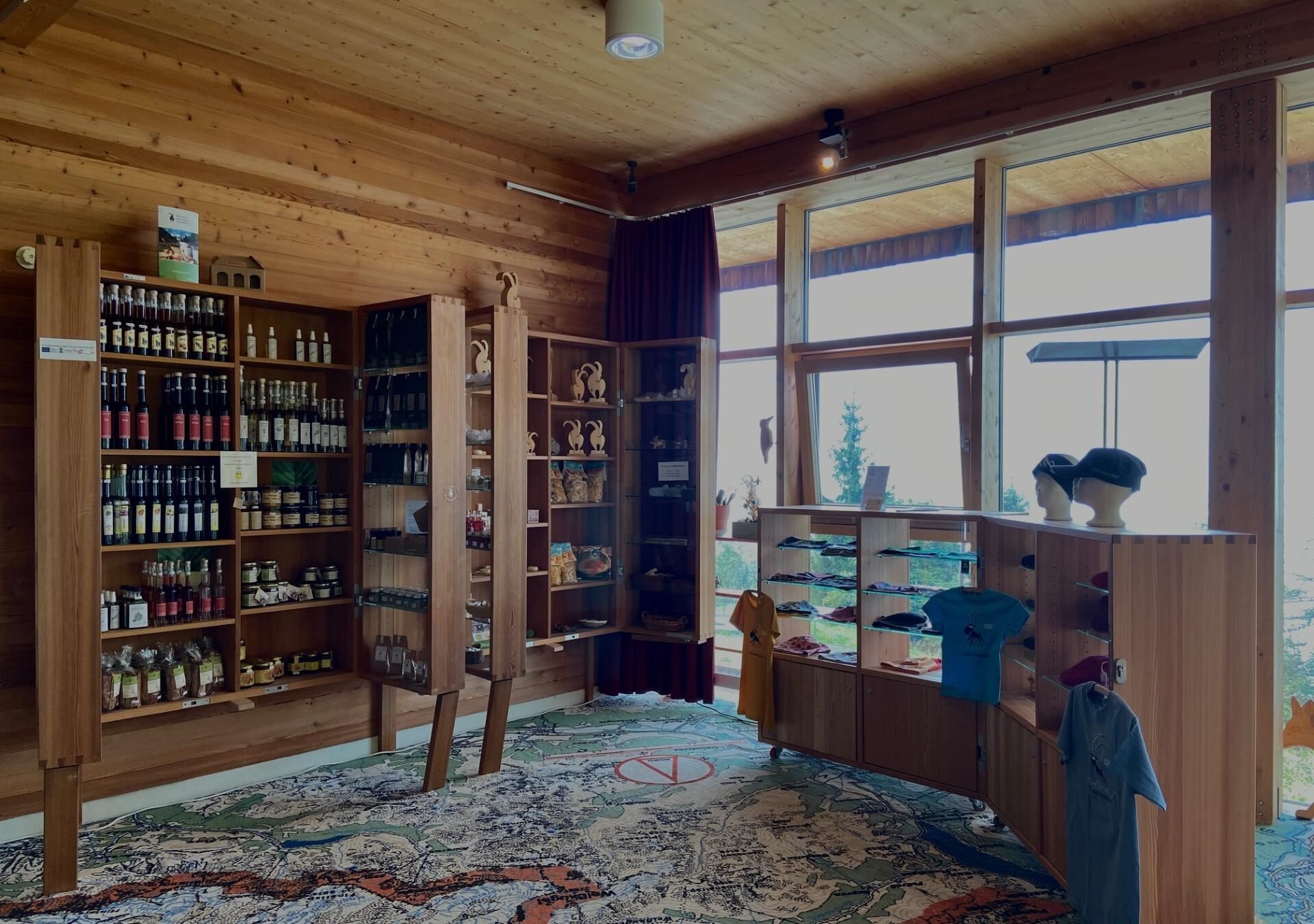 Ein gemütlicher Verkaufsraum mit Holzhregalen, gefüllt mit lokalen Produkten. Große Fenster bieten einen Blick nach draußen und viel Tageslicht.