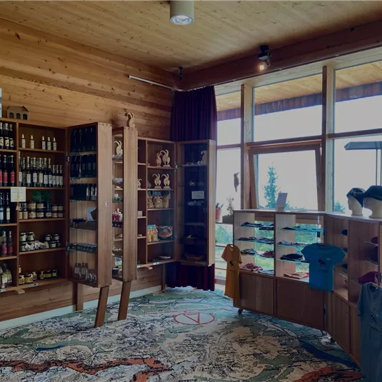 Ein gemütlicher Verkaufsraum mit Holzhregalen, gefüllt mit lokalen Produkten. Große Fenster bieten einen Blick nach draußen und viel Tageslicht.