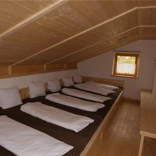 Ein gemütlicher, heller Raum mit Holzverkleidung. Auf der Seite befinden sich mehrere Matratzen mit Kissen.