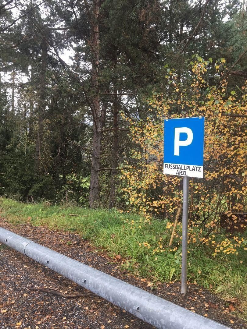 Ein Parkplatzschild für den Fußballplatz in Arzl. Im Hintergrund sind Bäume und herbstliche Blätter sichtbar.