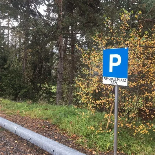 Ein Parkplatzschild für den Fußballplatz in Arzl. Im Hintergrund sind Bäume und herbstliche Blätter sichtbar.
