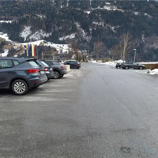 A parking lot with several cars in a rural setting. In the background, mountains and snow are visible.
