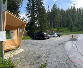Eine Haltestelle aus Holz in einer Waldumgebung. Weitere Autos sind auf einem geräumigen Parkplatz in der Nähe der Kurve abgestellt.