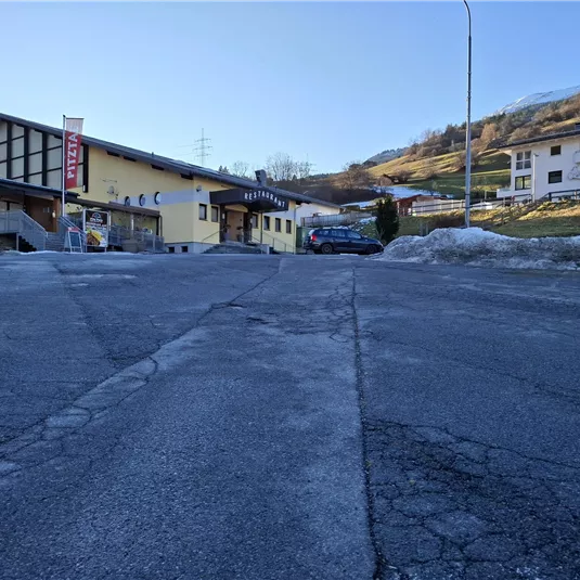 Eine ruhige Straße mit einem Hotel und einigen Wohngebäuden im Hintergrund. Im Vordergrund ist der Asphalt sichtbar, mit noch etwas Schnee an den Rändern.