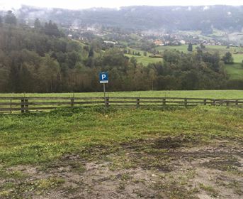 Eine grüne Wiese mit einem Parkplatzschild. Im Hintergrund sieht man sanfte Hügel und einen kleinen Ort.
